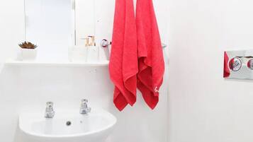 A bathroom with a white sink, two faucets, and a mirror. There are two red towels hanging on a towel rack.