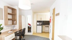 Un espacio habitable compacto con kitchenette, un escritorio y una silla, y una pequeña zona de comedor.
