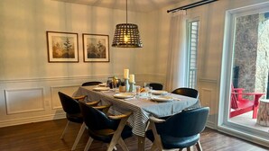 Un'area pranzo con un tavolo apparecchiato per quattro persone, circondata da sedie scure, un lampadario e quadri appesi al muro.