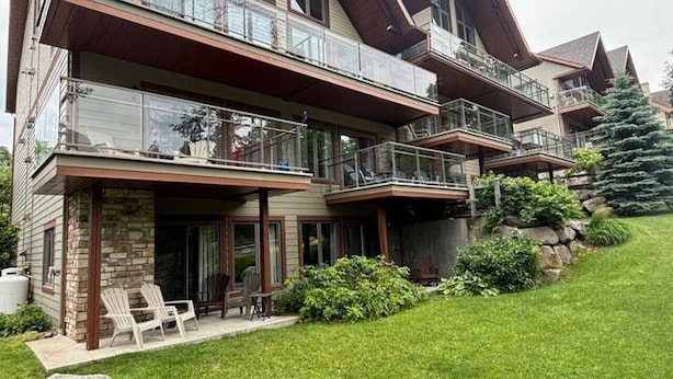 Une maison à plusieurs étages dotée d’un balcon, d’une façade en pierre et d’une pelouse bien entretenue.