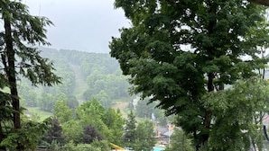 Un balcon avec une table et des chaises, donnant sur un paysage verdoyant, avec des arbres et une vue lointaine sur une ville.