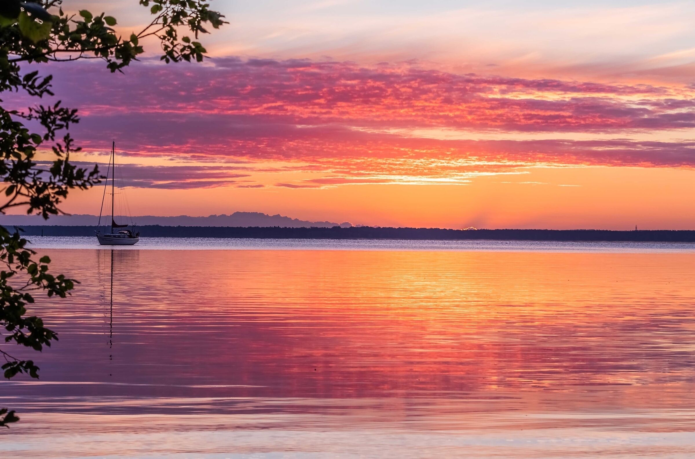 A calm body of water with a sailboat anchored in the distance, surrounded by a natural landscape.