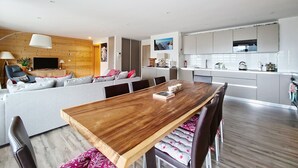 Un espace de vie moderne comprenant une table à manger en bois, un canapé avec des coussins, un téléviseur et un coin cuisine avec des placards et des appareils électroménagers.