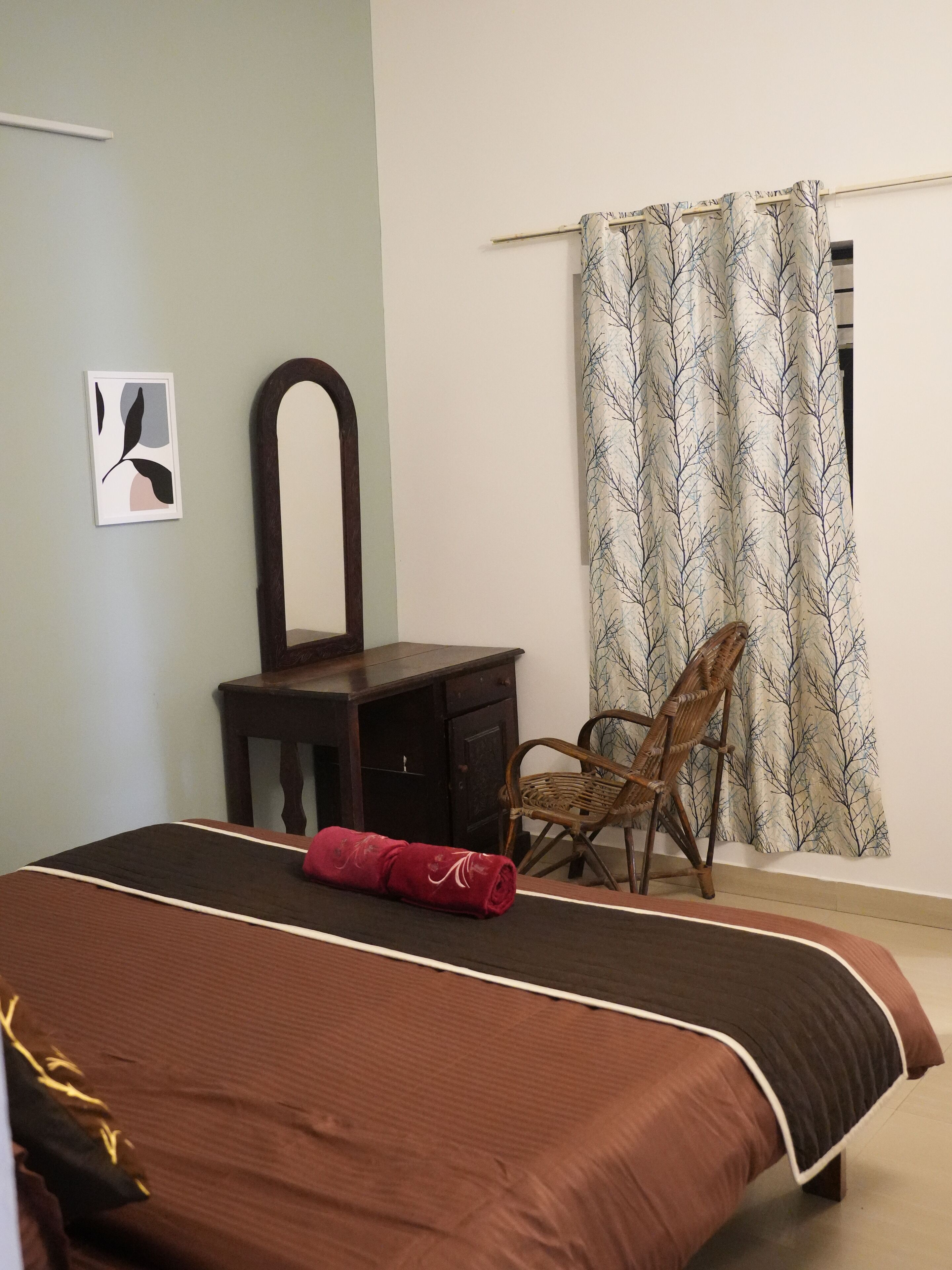 A bedroom with a large bed, a wooden dresser, a chair, a mirror, and a curtain with a tree pattern.