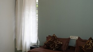 A bedroom with a bed, pillows, a bedside table, a bottle, a curtain, and an air conditioning unit. -  Kulture KonnectT North Cliff" (Varkala)