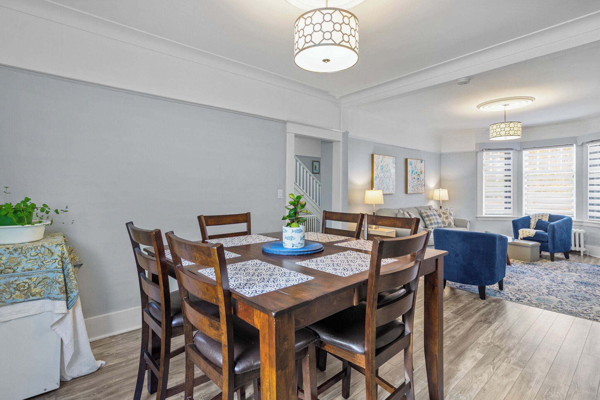A dining area with a wooden table, chairs, and a vase with a plant. There is a staircase leading to another room.
