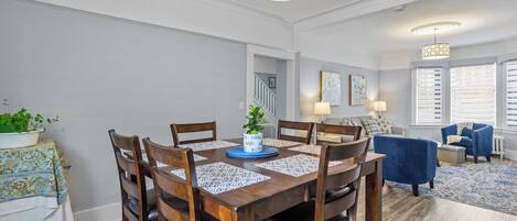 A dining area with a wooden table, chairs, and a vase with a plant. There is a staircase leading to another room.