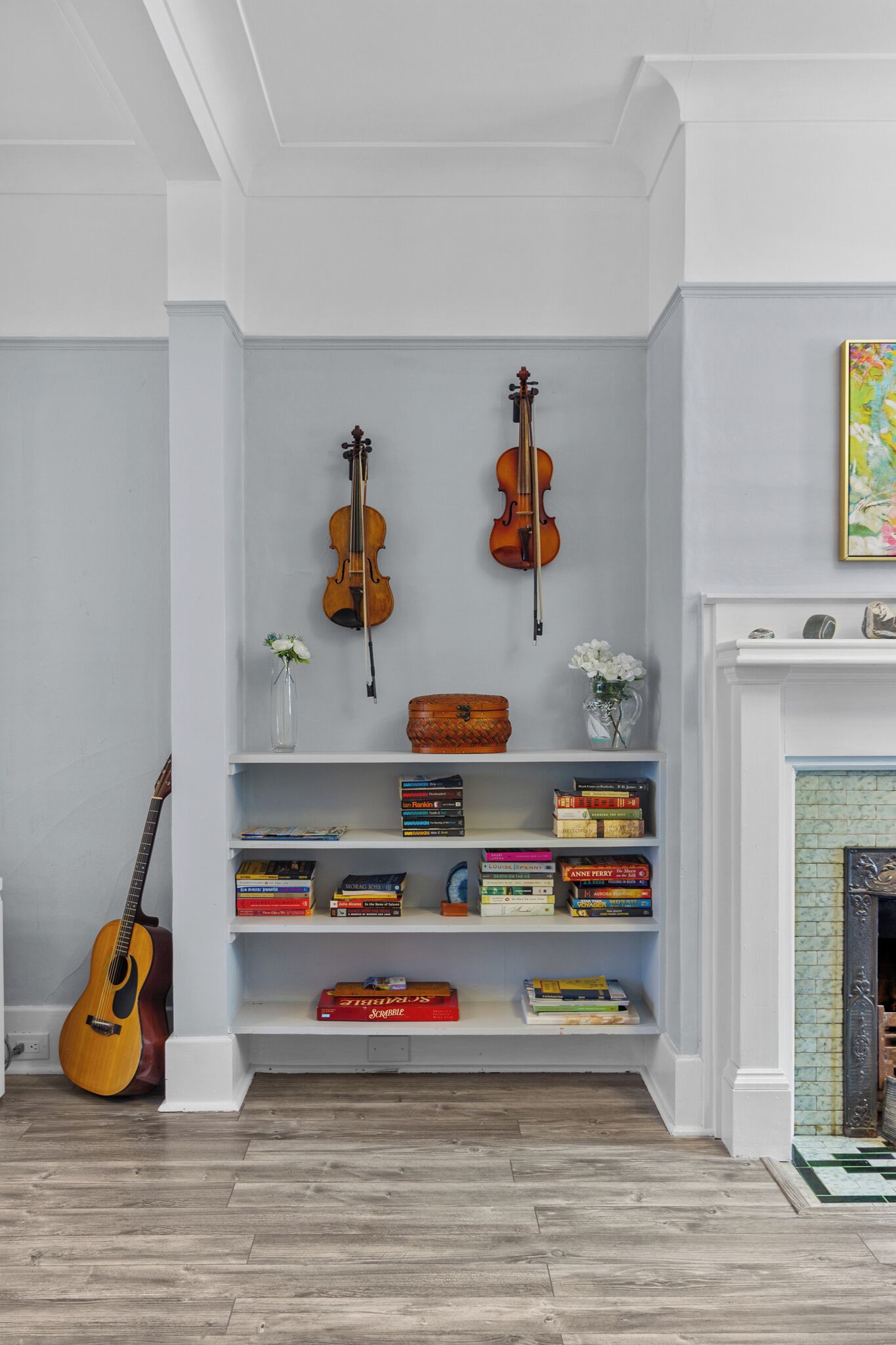 Ein Zimmer mit weißer Wand, einem Kamin, einem Bücherregal mit Büchern sowie einer Geige und einer Gitarre.