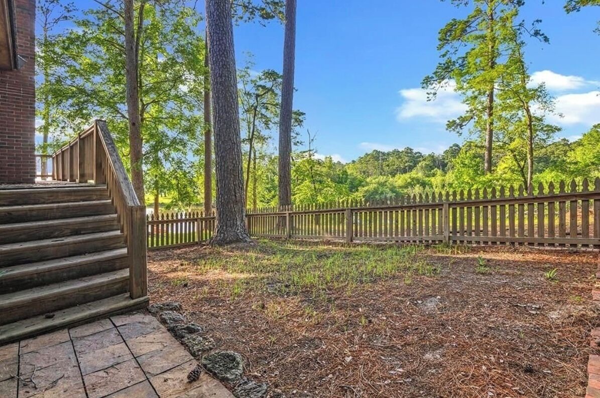 A wooden staircase leading to a porch, surrounded by a wooden fence and tall trees.