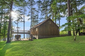 A wooden cabin with a deck and a boat docked outside, surrounded by trees and a clear sky. - Terrific cabin on Lake Sam Rayburn (Broaddus)