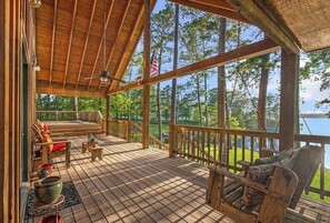 A wooden deck with outdoor seating, a flag, and a view of trees and water. - Terrific cabin on Lake Sam Rayburn (Broaddus)