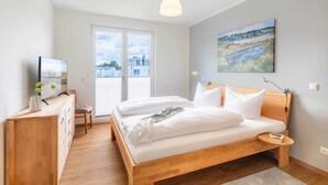 Un dormitorio con cama, mesita de noche, lámpara y un cuadro en la pared.