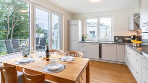 Una cocina moderna con armarios blancos, una mesa de comedor de madera para cuatro personas y grandes ventanales con vistas al exterior.
