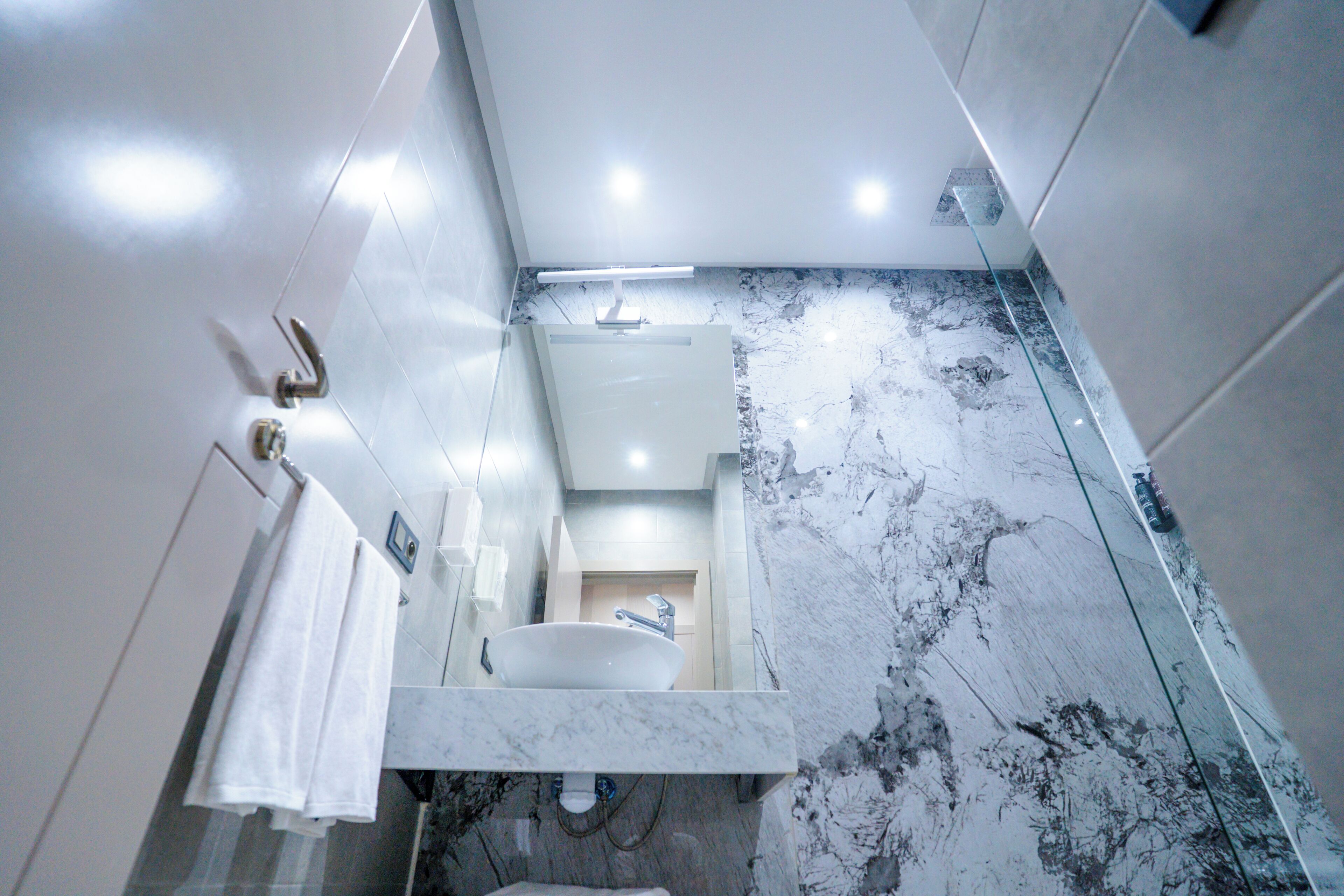 A modern bathroom with a marble sink, white walls, and a glass shower enclosure.