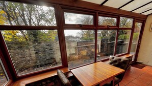 A room with a wooden table and bench by a large window overlooking a stone wall and trees. - Gorgeous Cottage in Stoke-on-Trent's "village in the city" - Penkhull (Stoke-on-Trent)