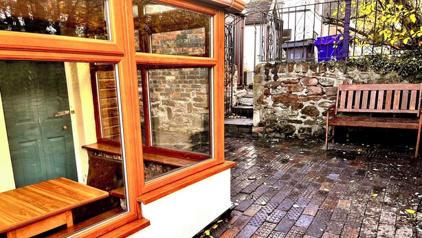 A wooden bench outside a building with large windows, a stone wall, and a wet brick floor. - Gorgeous Cottage in Stoke-on-Trent's "village in the city" - Penkhull (Stoke-on-Trent)