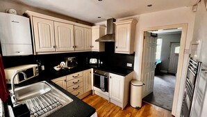 A compact kitchen with white cabinetry, a black countertop, and a stainless steel sink. - Gorgeous Cottage in Stoke-on-Trent's "village in the city" - Penkhull (Stoke-on-Trent)