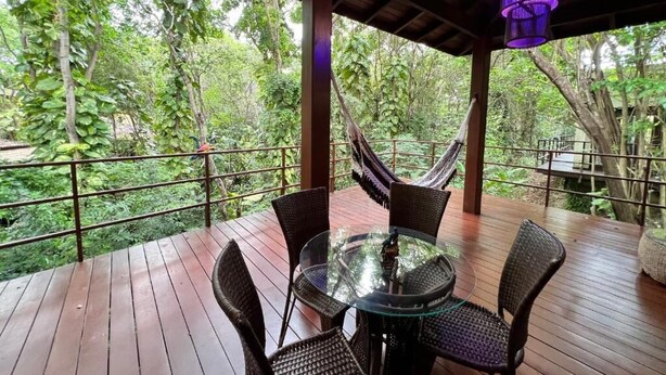 A wooden deck with a glass table and wicker chairs, surrounded by lush greenery and a hammock. - Pipa Blue (Tibau do Sul)
