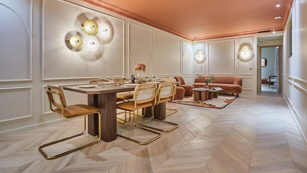 Zona pranzo moderna con tavolo in legno, sedie dorate e parete decorata con applique.