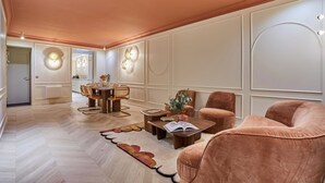 Un ampio soggiorno con pavimento in parquet a spina di pesce, un tavolo da pranzo rotondo con sedie, un comodo divano rosa e un tavolino da caffè.
