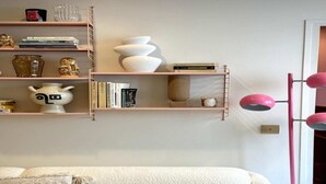 Un salón con sofá, una lámpara rosa y estanterías con libros y objetos decorativos.