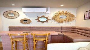 Una cocina moderna con un banco curvo rosa, dos taburetes de madera y espejos decorativos en la pared.