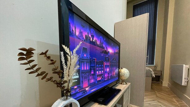 A flat-screen TV on a wooden TV stand with a decorative plant and a globe. - City Chic Apartment in Leeds (Leeds)