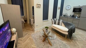 A modern living room with a sofa, a glass coffee table, and a TV. There is a kitchen area with a microwave and a clock on the wall. - City Chic Apartment in Leeds (Leeds)