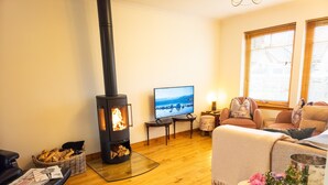 A cozy living room with a wood-burning stove, a television, a comfortable sofa, and a wooden floor. - Casa Amor - Aviemore (Aviemore)