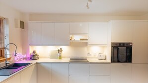 A modern kitchen with white cabinets, a built-in oven, and a neon sign. - Casa Amor - Aviemore (Aviemore)