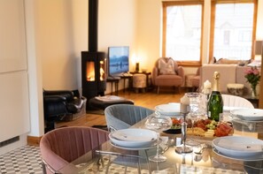 Un coin repas avec une table en verre dressée pour le repas, une cheminée et, au fond, un salon confortable.
