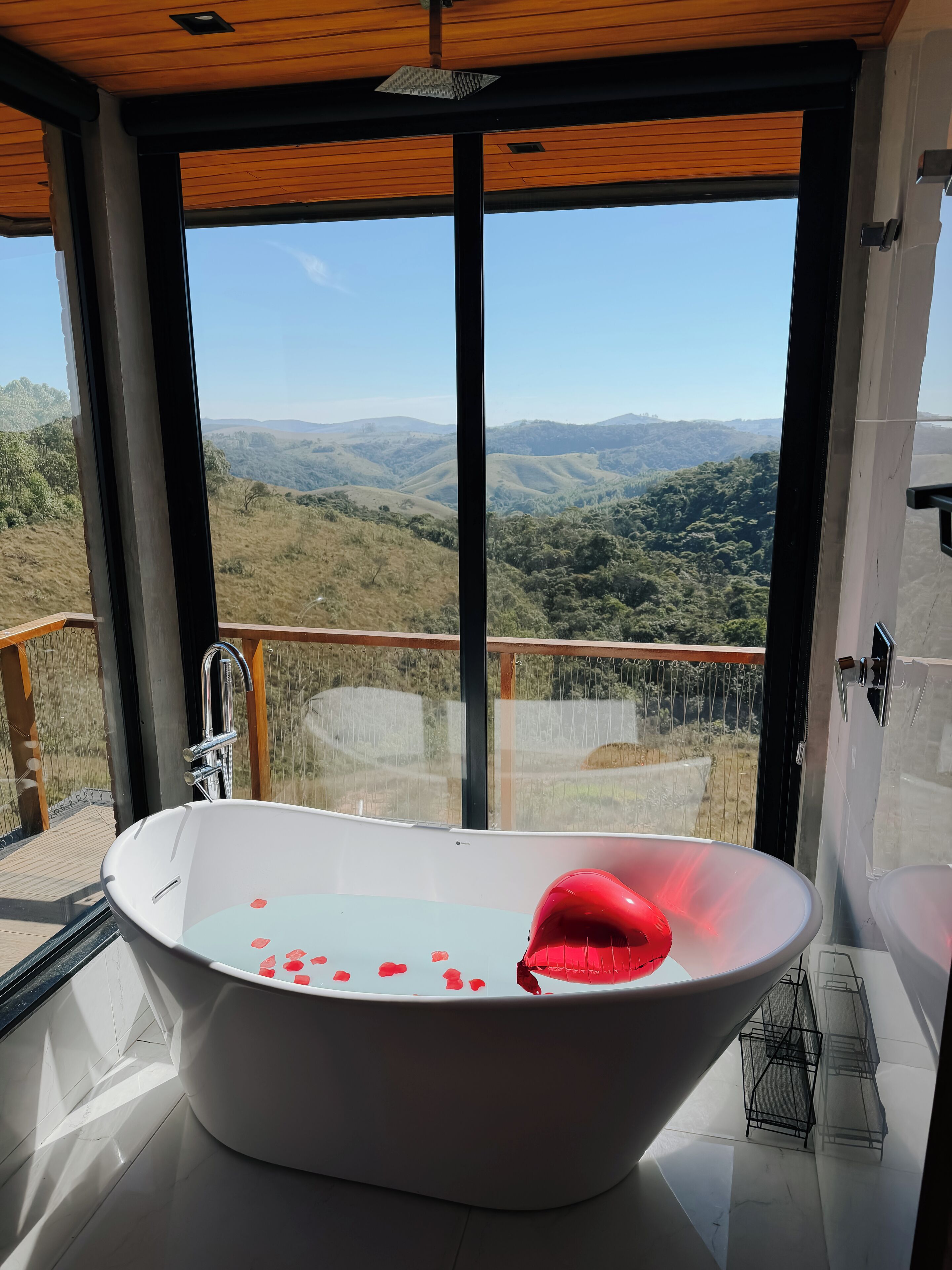 A modern bathroom with a large bathtub, a view of rolling hills, and a wooden ceiling.
