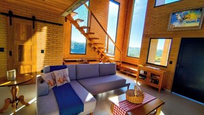 A modern living room with a large sofa, a wooden staircase, and large windows. - Ibitipoca Castle (Conceição da Ibitipoca)