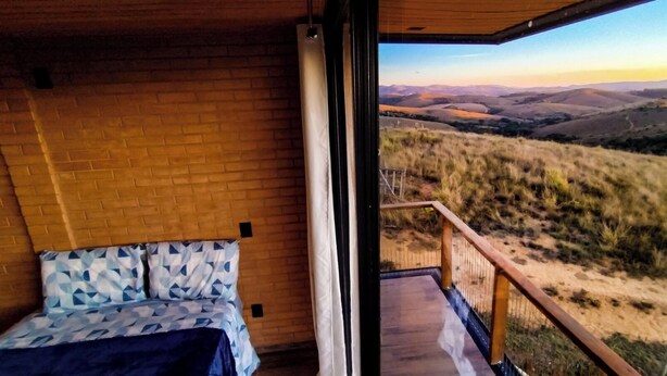 A bedroom with a bed and a balcony overlooking a hilly landscape. - Ibitipoca Castle (Conceição da Ibitipoca)