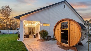 A house with a covered patio, a wooden barrel door, and a well-maintained lawn. - Modern Family Home | Sauna, Fire Pit, Swings & Access to Pools & Parks (Kuna)