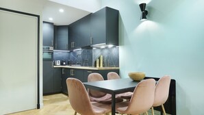 Cozinha moderna com armários escuros, painel de fundo de mármore e área de jantar com mesa preta e cadeiras cor de rosa.
