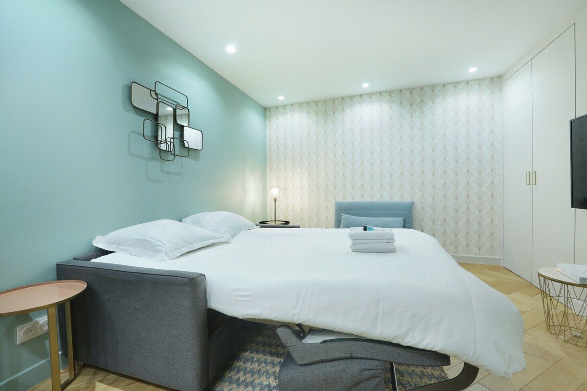 Ein modernes Schlafzimmer mit Bett, Nachttischen, einem Fernseher und einer Wand mit Muster.