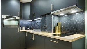 Cozinha moderna com armários escuros, painel de mármore e eletrodomésticos de aço inoxidável.