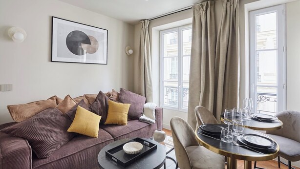 A modern living room with a sofa, a dining table set for two, and a large window with curtains. - New Apartment Center of Paris Le Marais (Paris)