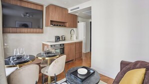 A modern kitchen with wooden cabinets, a built-in oven, and a dining area with round tables and chairs. - New Apartment Center of Paris Le Marais (Paris)