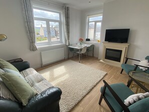 Ein Wohnzimmer mit Sofa, Esstisch, Fernseher und Kamin.