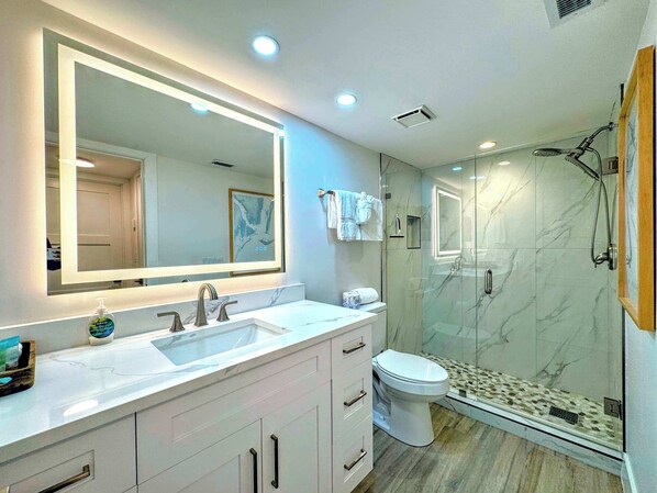 Een moderne badkamer met een grote spiegel, een wastafel, een toilet en een douchecabine met glazen wanden.