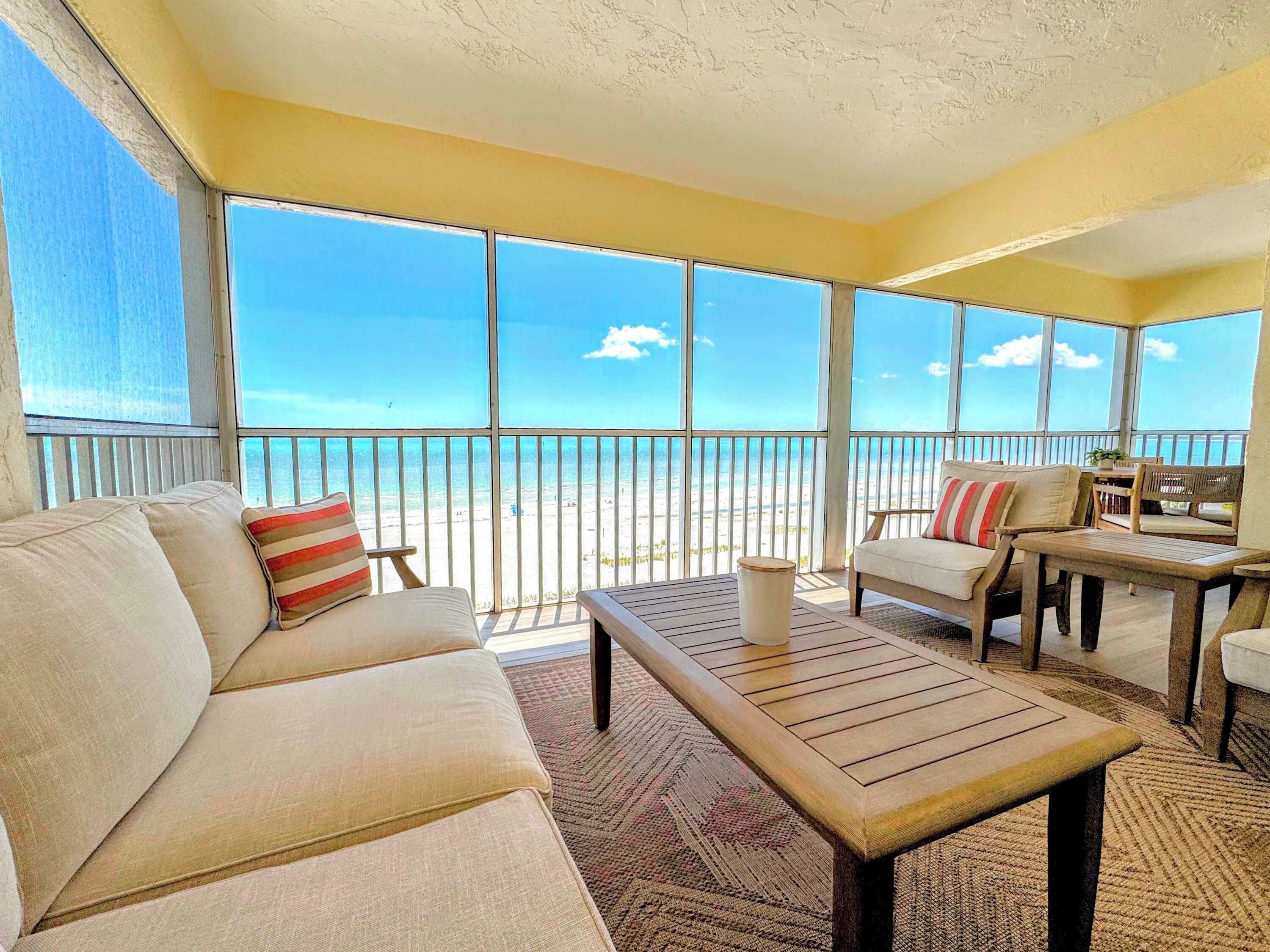 A balcony with a sofa, chairs, and a table, overlooking a beach.