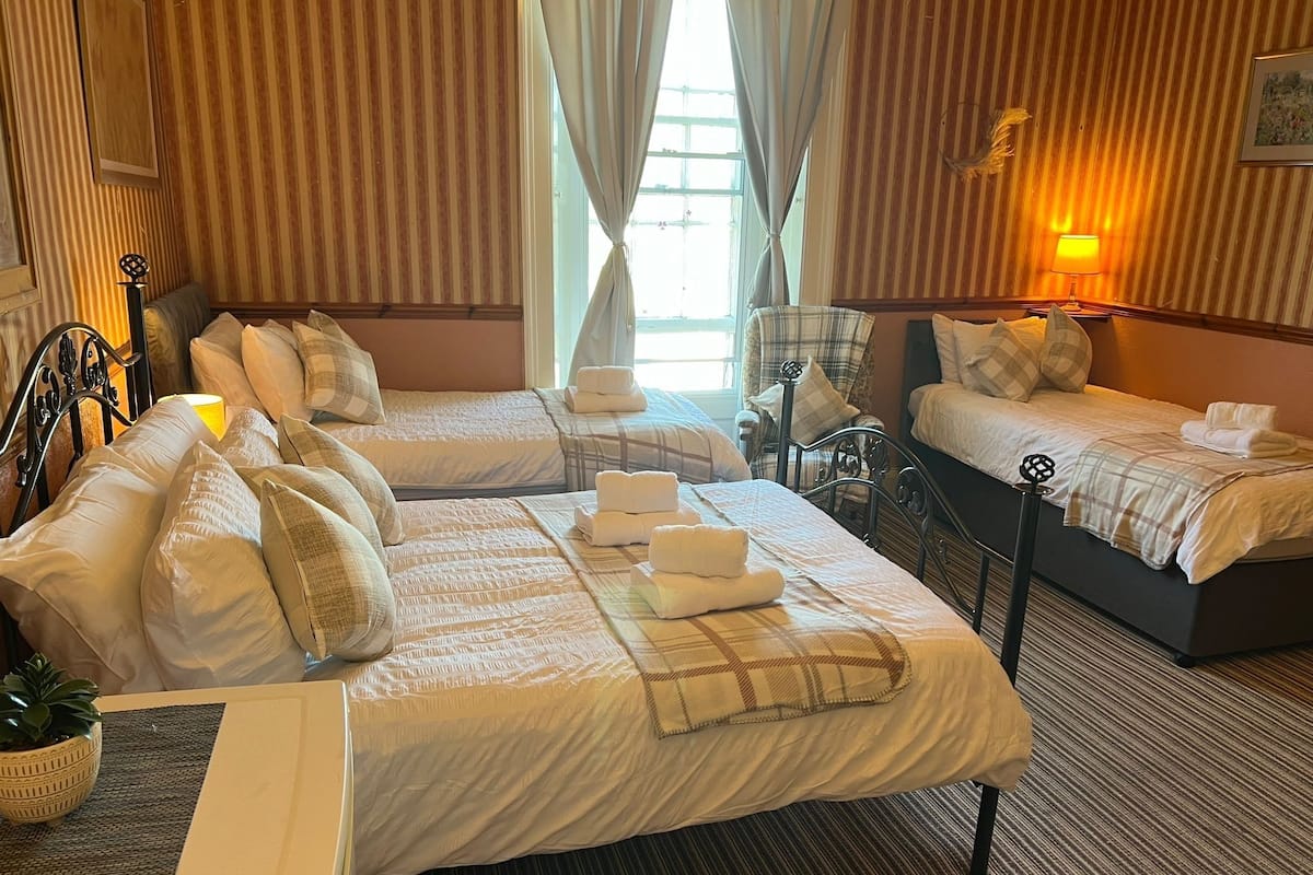 Une chambre d’hôtel avec deux lits, un bureau, une chaise, une lampe et une fenêtre avec des rideaux.
