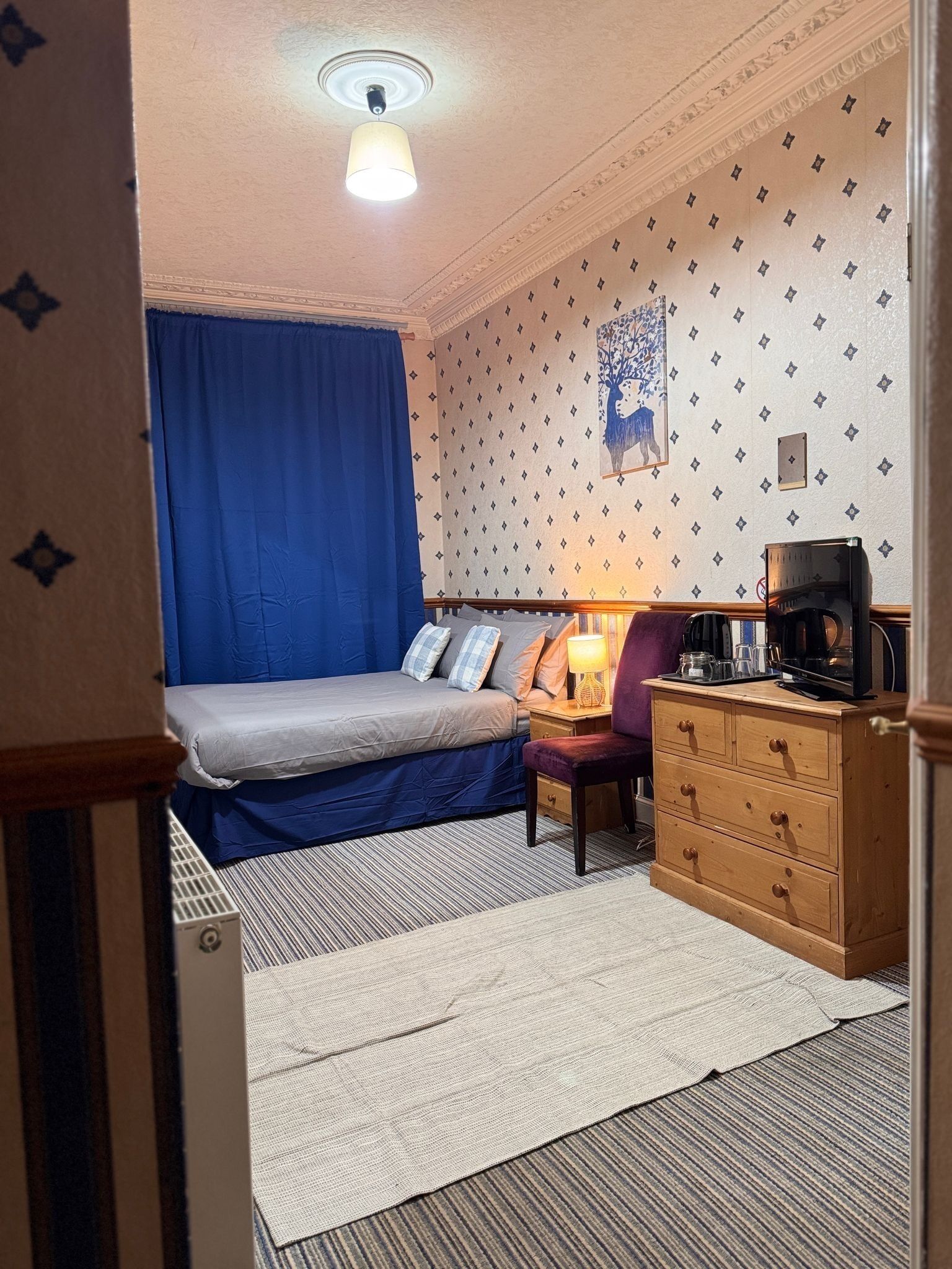 A bedroom with a bed, a dresser, a lamp, and a painting on the wall.