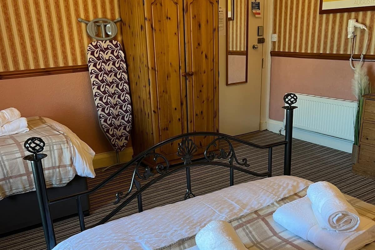 Une chambre d’hôtel avec deux lits, une armoire en bois, un radiateur et un tableau au mur.