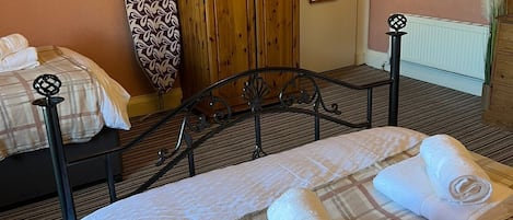 A hotel room with two beds, a wooden wardrobe, a radiator, and a painting on the wall.