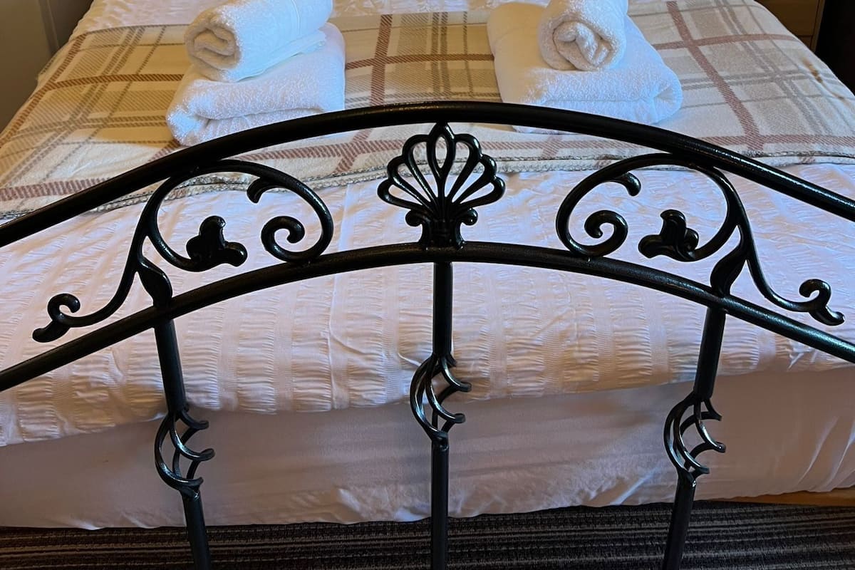 Un lit bien fait, avec une couverture à carreaux, plusieurs oreillers et des serviettes enroulées.