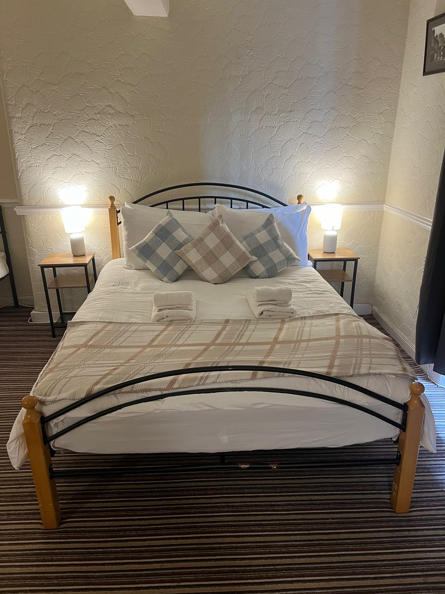 Un lit bien fait, recouvert d’une couvre-lit à carreaux, avec deux lampes de chevet et un mur à texture.