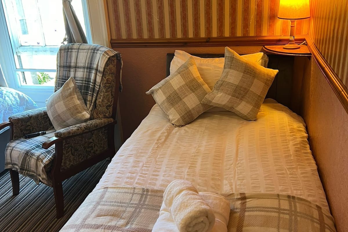 Une chambre d’hôtel avec un lit, une chaise, une lampe et une fenêtre.
